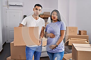 Young hispanic couple expecting a baby moving to a new home puffing cheeks with funny face