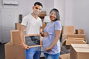Young hispanic couple expecting a baby moving to a new home smiling with a happy and cool smile on face