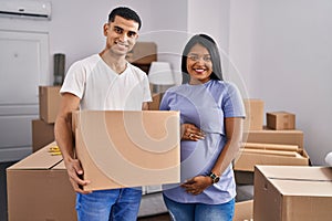 Young hispanic couple expecting a baby moving to a new home smiling with a happy and cool smile on face