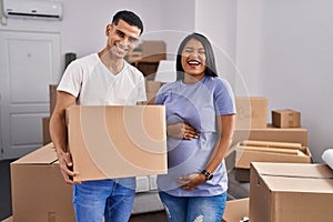 Young hispanic couple expecting a baby moving to a new home smiling and laughing hard out loud because funny crazy joke