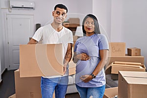 Young hispanic couple expecting a baby moving to a new home smiling looking to the side and staring away thinking