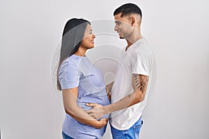 Young hispanic couple expecting a baby standing over background looking to side, relax profile pose with natural face and