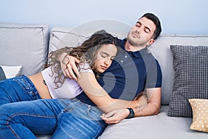 Young hispanic couple hugging each other lying on sofa sleeping at home