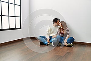 Young hispanic couple kissing and sitting on the floor at empty new home