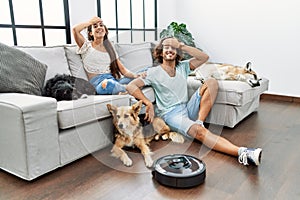 Young hispanic couple relaxing at home by vacuum robot stressed and frustrated with hand on head, surprised and angry face