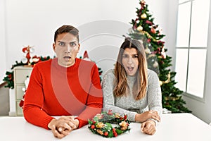 Young hispanic couple sitting at the table on christmas afraid and shocked with surprise expression, fear and excited face