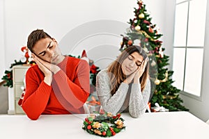 Young hispanic couple sitting at the table on christmas sleeping tired dreaming and posing with hands together while smiling with