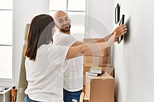 Young hispanic couple smiling happy hanging picture on wall at new home