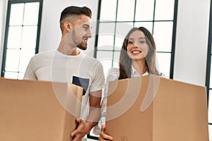 Young hispanic couple smiling happy holding cardboard boxes moving at new home