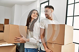 Young hispanic couple smiling happy holding cardboard boxes moving at new home