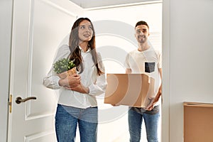 Young hispanic couple smiling happy holding cardboard boxes moving at new home