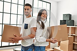 Young hispanic couple smiling happy holding cardboard boxes moving at new home