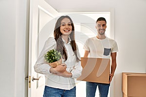 Young hispanic couple smiling happy holding cardboard boxes moving at new home