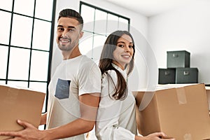 Young hispanic couple smiling happy holding cardboard boxes moving at new home