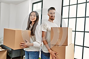 Young hispanic couple smiling happy holding cardboard boxes moving at new home