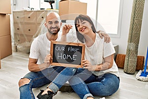 Young hispanic couple smiling happy holding our new home blackboard and key at new home
