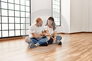 Young hispanic couple smiling happy reading book at empty new home