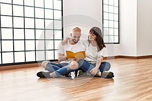 Young hispanic couple smiling happy reading book at empty new home