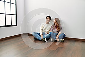 Young hispanic couple smiling happy sitting on the floor at empty new home