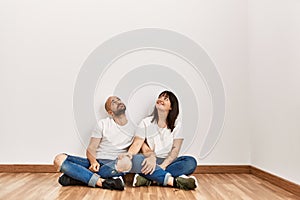 Young hispanic couple smiling happy sitting on the floor at empty new home