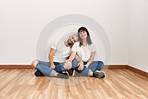 Young hispanic couple smiling happy sitting on the floor at empty new home