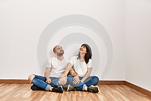 Young hispanic couple smiling happy sitting on the floor at empty new home