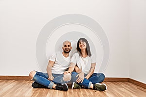 Young hispanic couple smiling happy sitting on the floor at empty new home