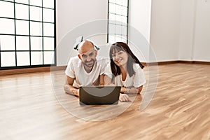 Young hispanic couple smiling happy using laptop at empty new home