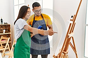 Young hispanic couple smiling happy using smartphone at art studio