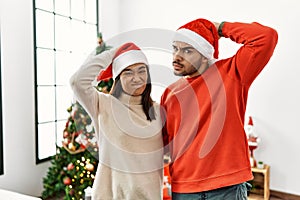 Young hispanic couple standing by christmas tree confuse and wondering about question