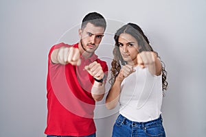 Young hispanic couple standing over isolated background punching fist to fight, aggressive and angry attack, threat and violence