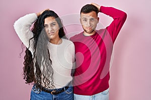 Young hispanic couple standing over pink background confuse and wondering about question