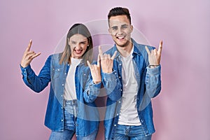 Young hispanic couple standing over pink background shouting with crazy expression doing rock symbol with hands up