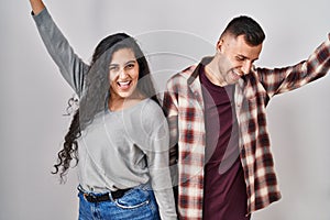 Young hispanic couple standing over white background dancing happy and cheerful, smiling moving casual and confident listening to