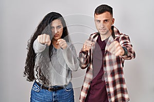 Young hispanic couple standing over white background punching fist to fight, aggressive and angry attack, threat and violence