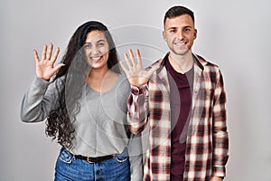 Young hispanic couple standing over white background showing and pointing up with fingers number ten while smiling confident and