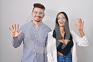 Young hispanic couple standing over white background showing and pointing up with fingers number ten while smiling confident and