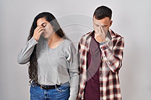 Young hispanic couple standing over white background tired rubbing nose and eyes feeling fatigue and headache