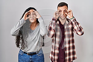 Young hispanic couple standing over white background trying to open eyes with fingers, sleepy and tired for morning fatigue