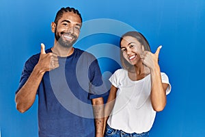 Young hispanic couple standing together doing happy thumbs up gesture with hand