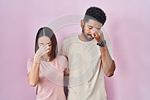 Young hispanic couple together over pink background tired rubbing nose and eyes feeling fatigue and headache