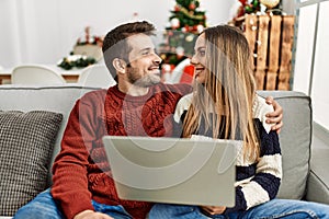 Young hispanic couple using laptop sitting on the sofa at home