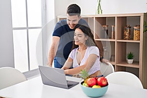 Young hispanic couple using laptop sitting on table at home