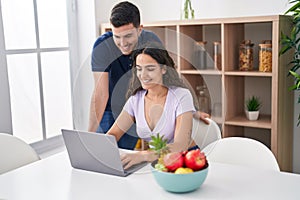Young hispanic couple using laptop sitting on table at home