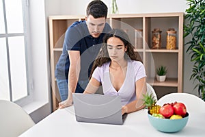 Young hispanic couple using laptop sitting on table at home