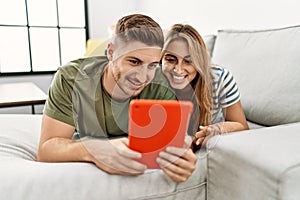 Young hispanic couple using touchpad lying on the sofa at home