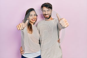 Young hispanic couple wearing casual clothes approving doing positive gesture with hand, thumbs up smiling and happy for success