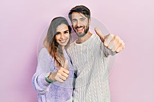 Young hispanic couple wearing casual clothes approving doing positive gesture with hand, thumbs up smiling and happy for success
