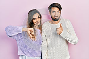 Young hispanic couple wearing casual clothes doing thumbs up and down, disagreement and agreement expression