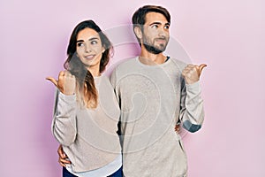 Young hispanic couple wearing casual clothes smiling with happy face looking and pointing to the side with thumb up